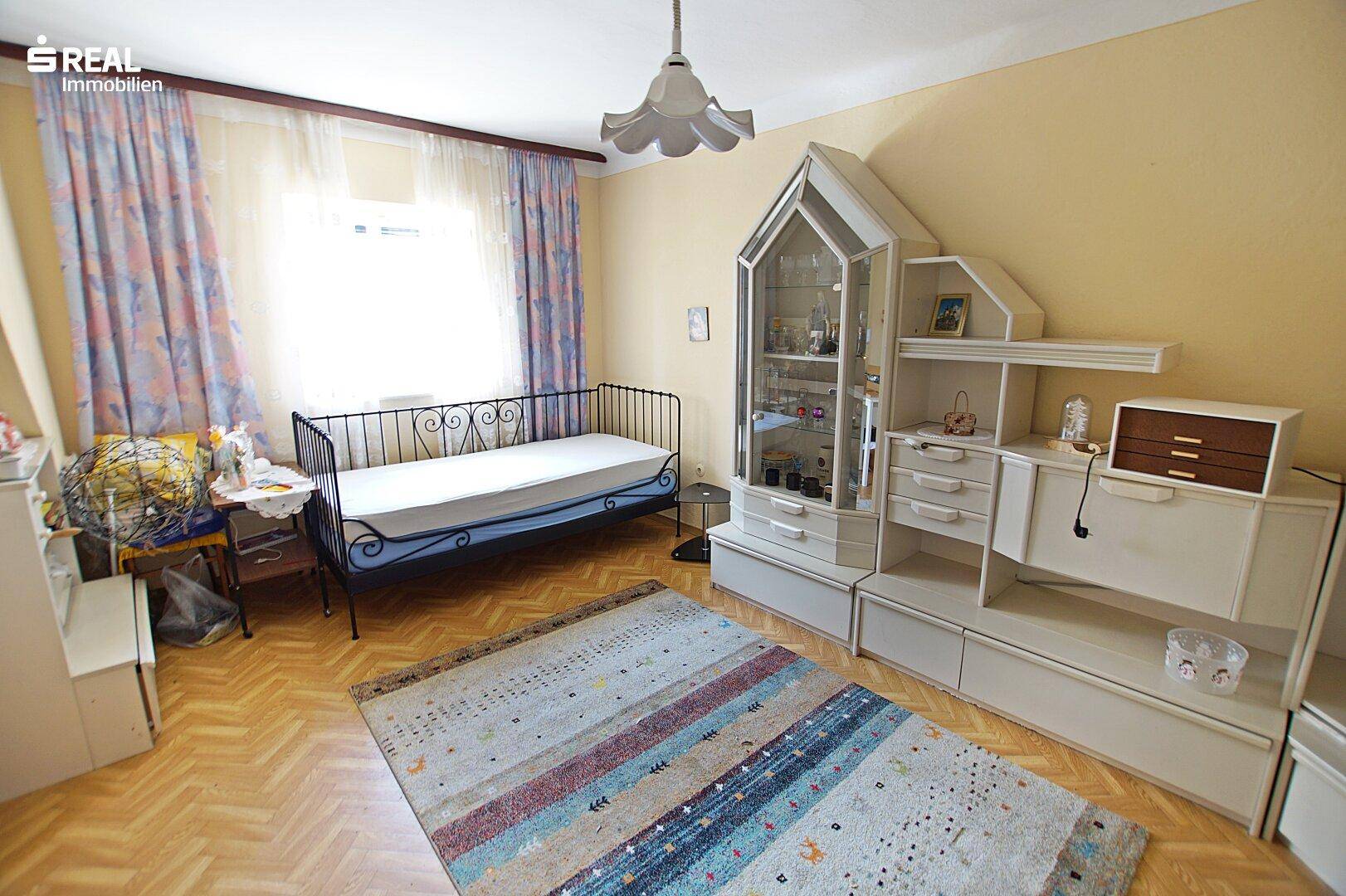 Schlafzimmer mit Einzelbett, Teppich und Schrankwand mit Vitrine.