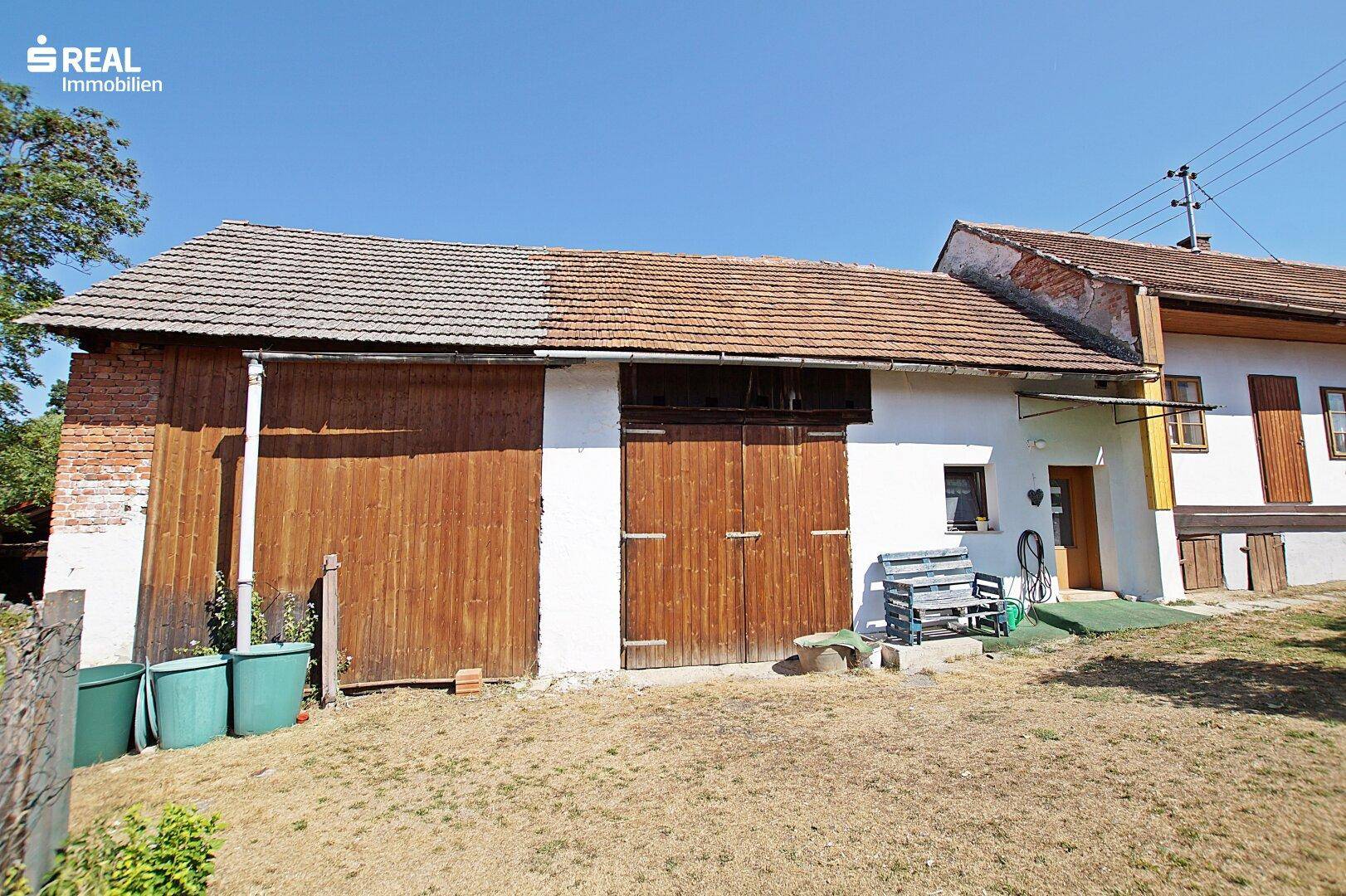Scheune mit Holztoren und Ziegeldach neben dem Wohnhaus.