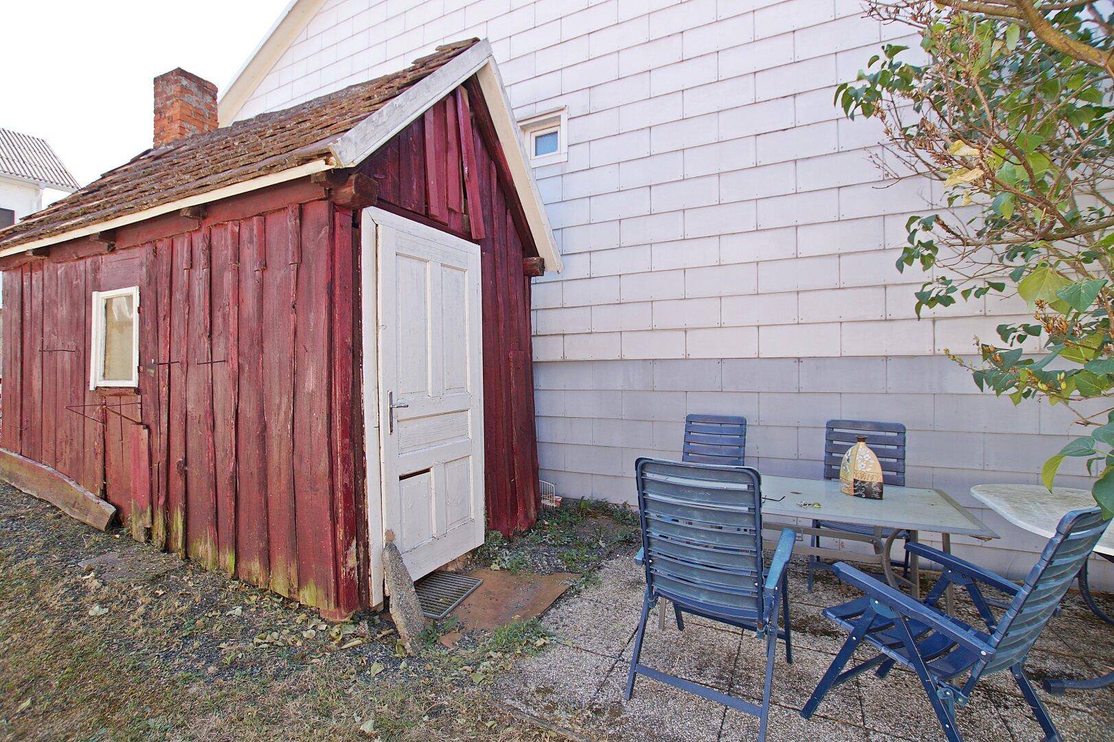 Kleine Terrasse mit Gartenmöbeln neben einem roten Holzschuppen.
