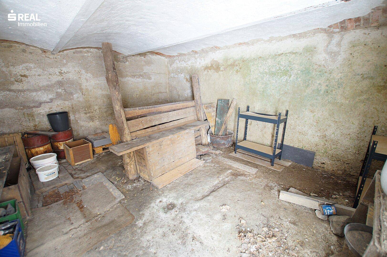 Alter Kellerraum mit Betonboden und einfachen Holzregalen.