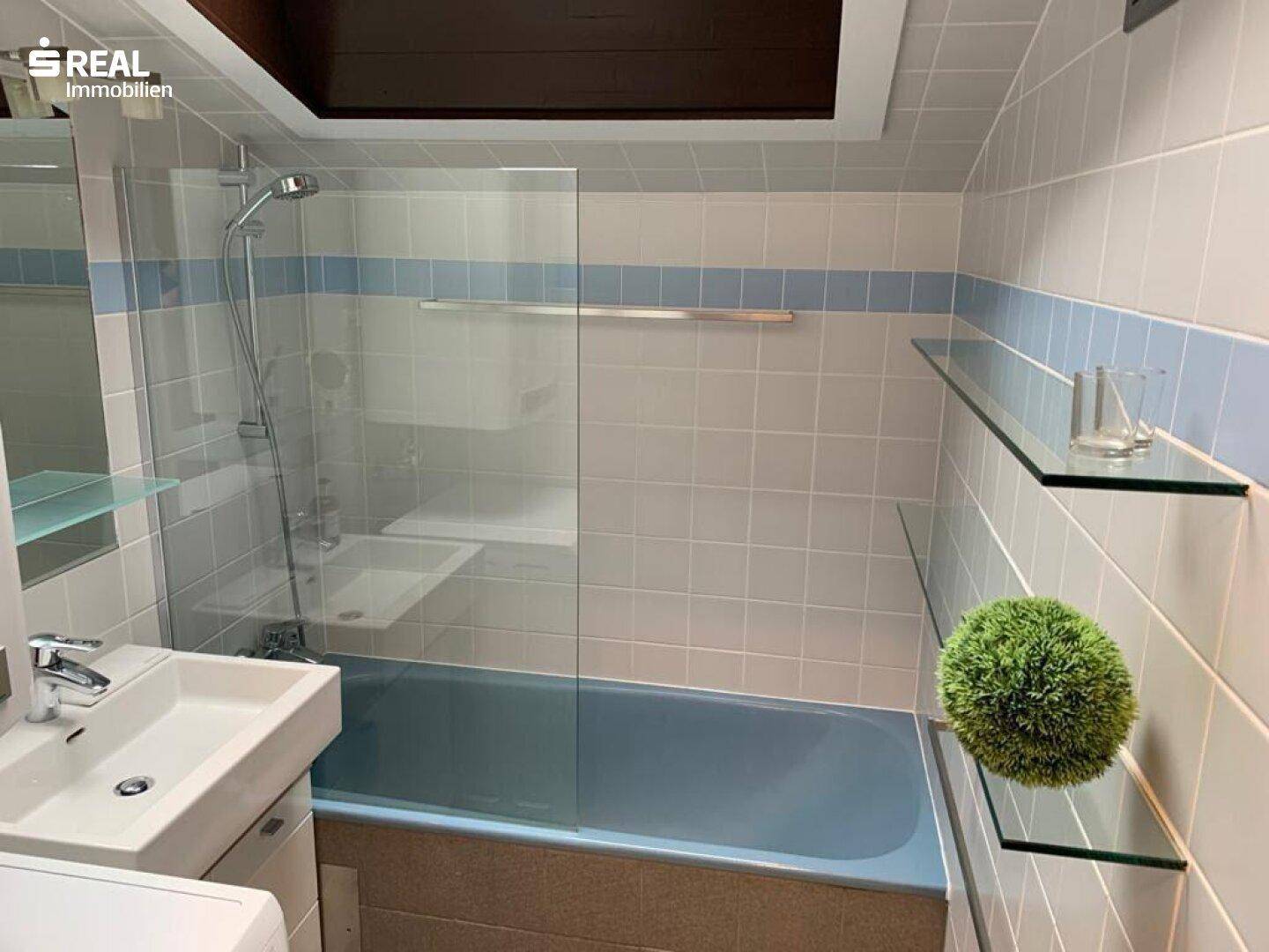 Badezimmer mit blauer Badewanne, Duschabtrennung und hellen Fliesen.