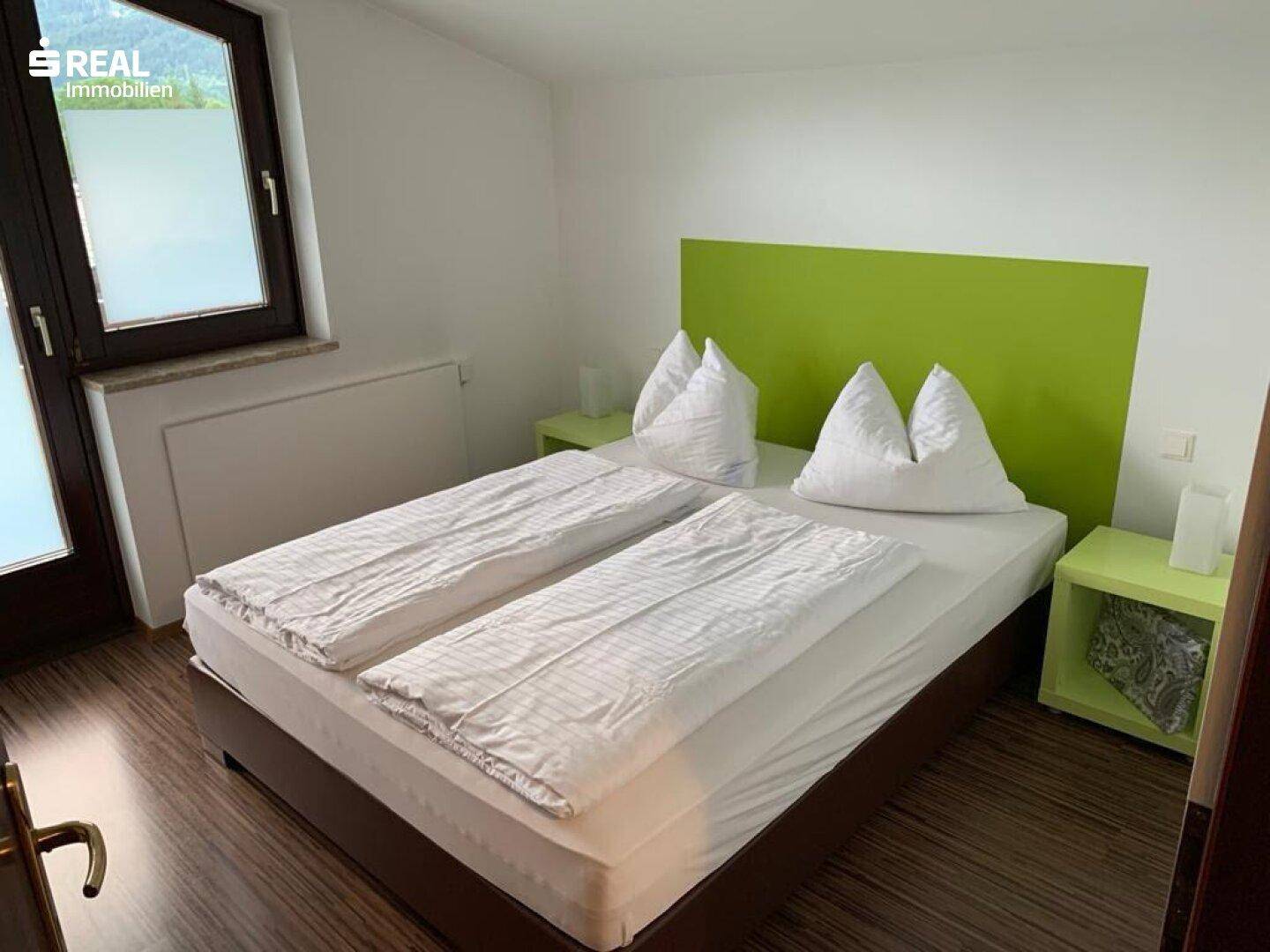 Helles Schlafzimmer mit Doppelbett, grünem Kopfteil und Holzboden.