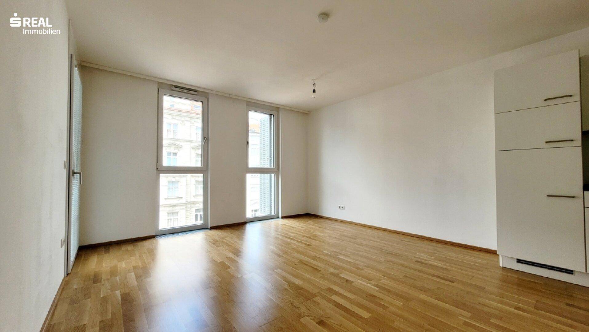Geräumiger Wohnbereich mit großen Fenstern und hellem Parkettboden.