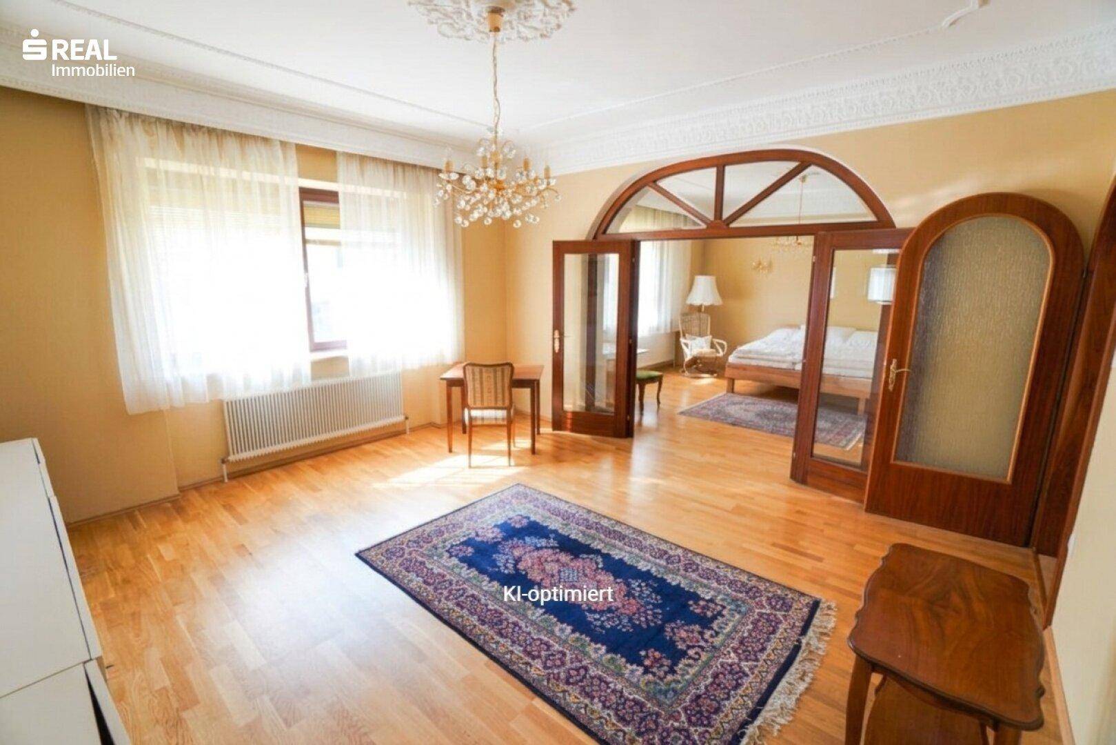 Helles Wohnzimmer mit Parkettboden, Stuckdecke und einem Durchgang zu einem weiteren Raum.
