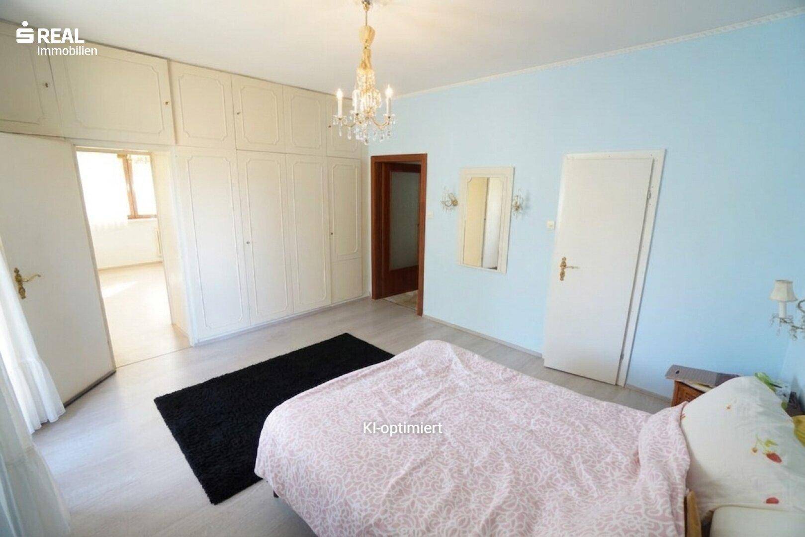 Geräumiges Schlafzimmer mit hellblauen Wänden, Einbauschränken und Zugang zu einem weiteren Raum.