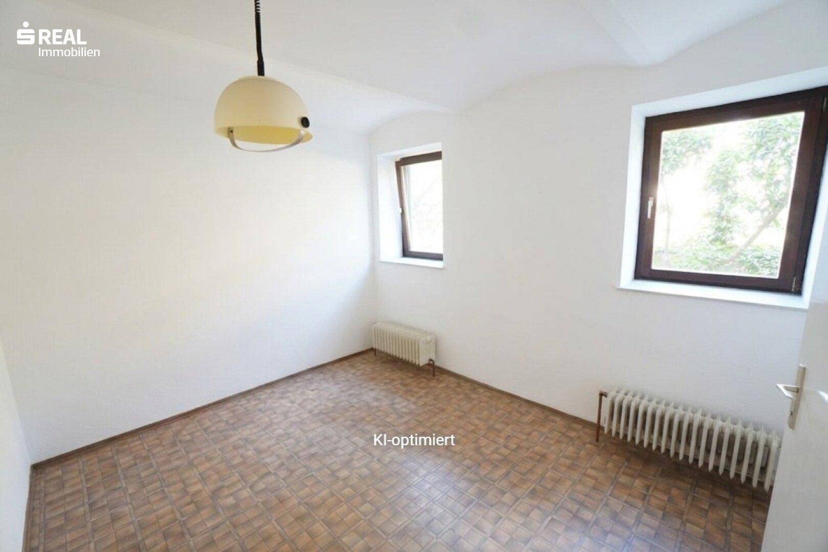 Helles Zimmer mit weißen Wänden, gemustertem Boden und zwei Fenstern.
