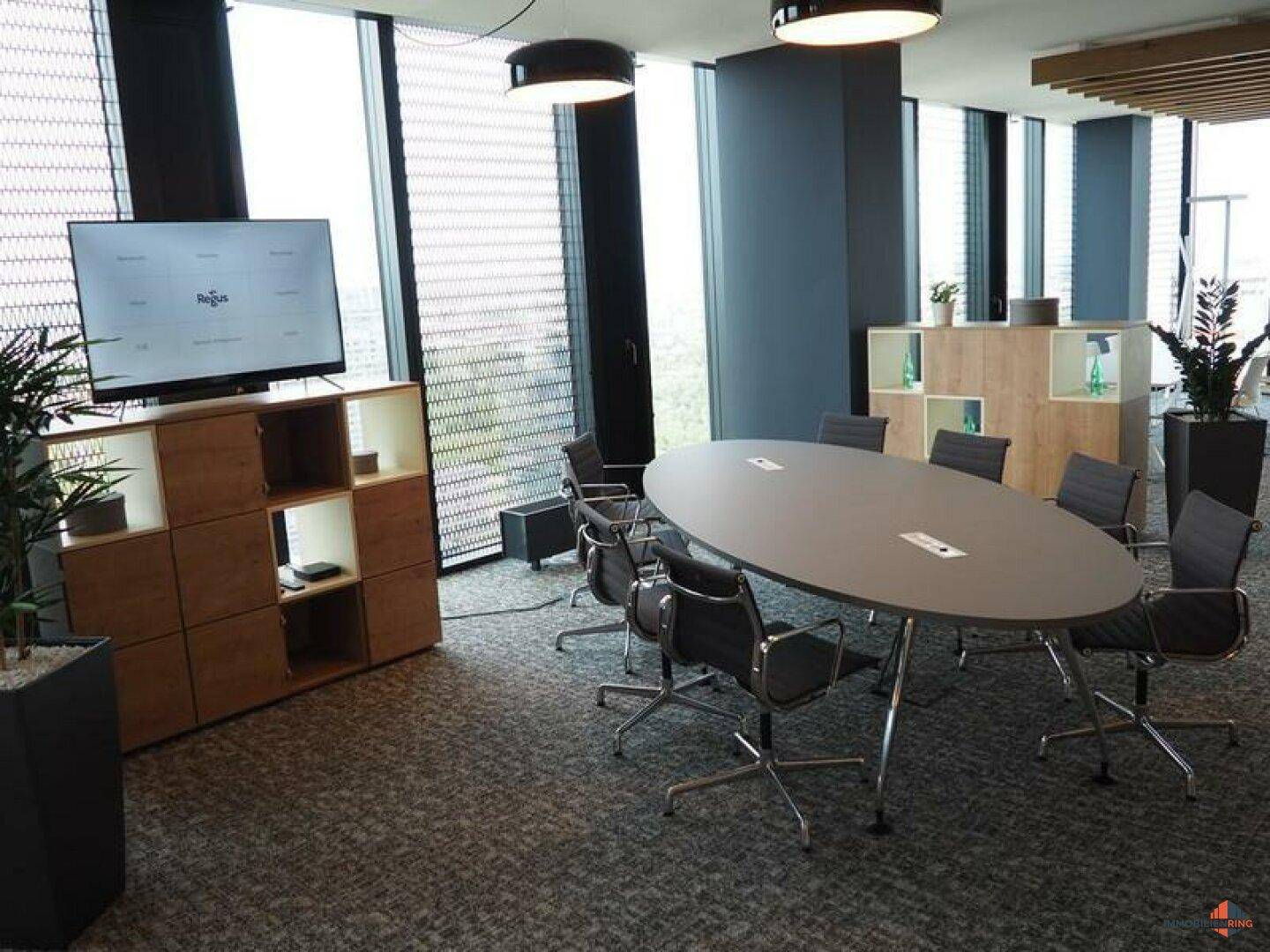 Eleganter Konferenzraum mit ovalem Tisch, Multimedia-Bildschirm und Blick auf die Umgebung.