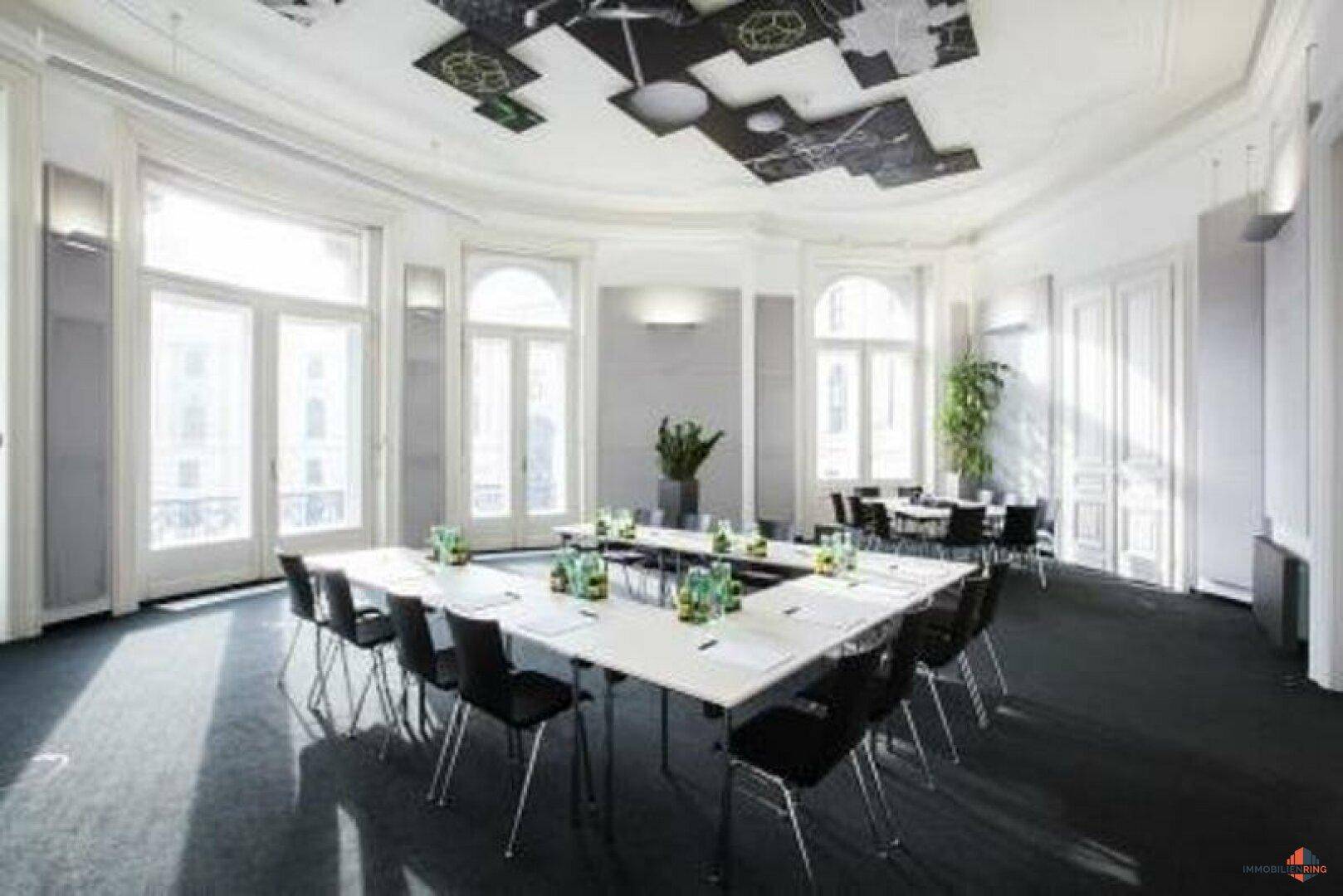 Geräumiger Konferenzraum mit einem großen Besprechungstisch, vielen Stühlen und dekorativen Deckenpaneelen.