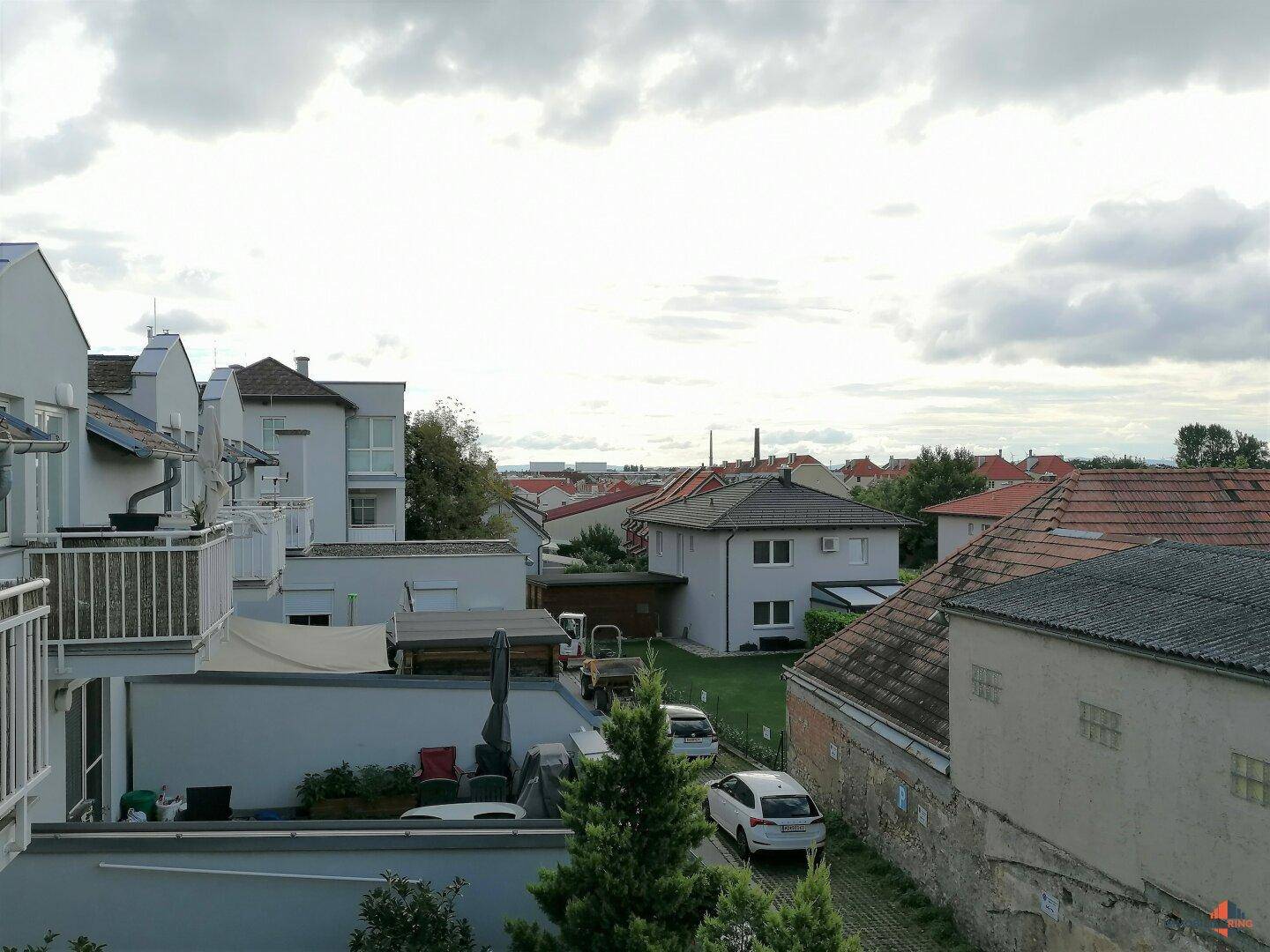 Blick über eine ruhige Wohngegend mit Häusern, Gärten und parkenden Autos unter bewölktem Himmel.