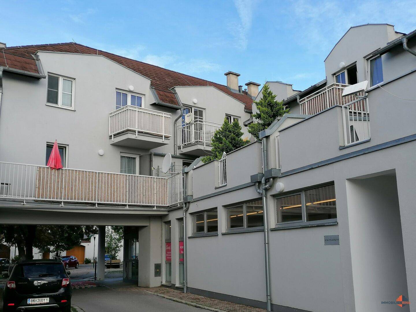 Wohngebäude mit mehreren Balkonen und einem Durchgang zu einem Innenhof, architektonisch ansprechend.
