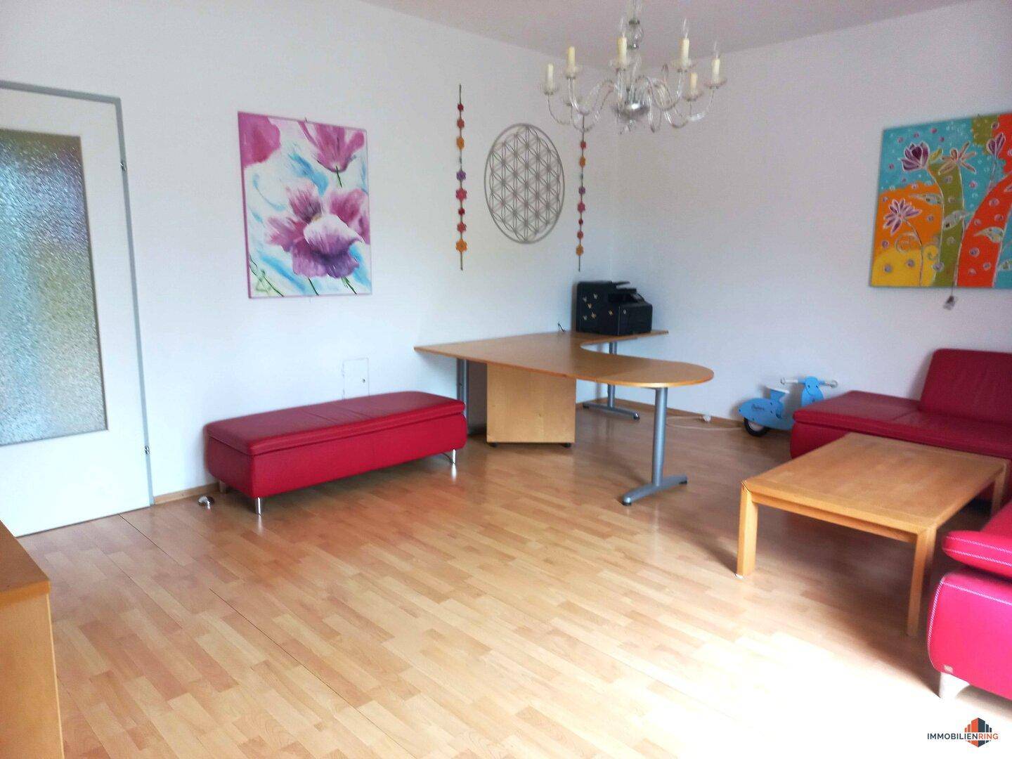 Heller Wohnbereich mit Holzboden, Schreibtisch und farbenfrohen Kunstwerken an der Wand.