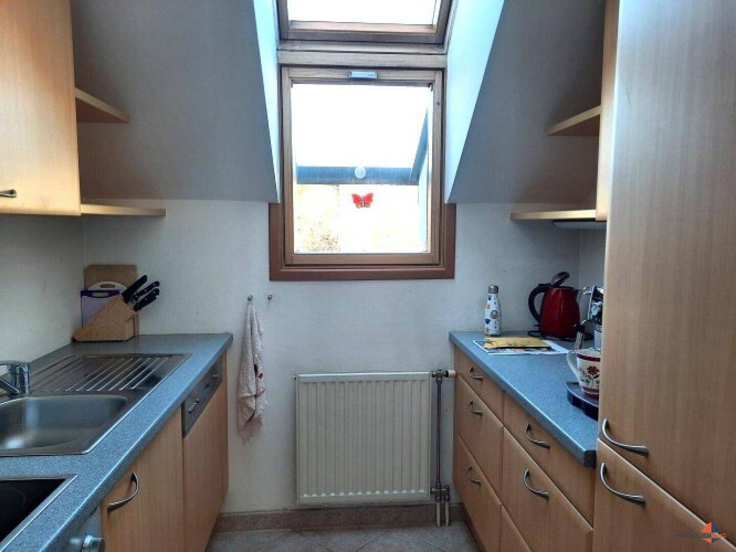 Kleine Küche im Dachgeschoss mit Dachfenster, Holzschränken und blauer Arbeitsplatte.