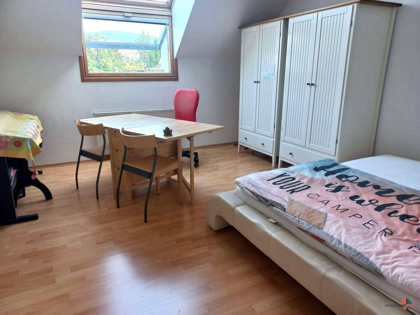 Schlafzimmer im Dachgeschoss mit Holzboden, Dachfenster und Blick auf die Landschaft.