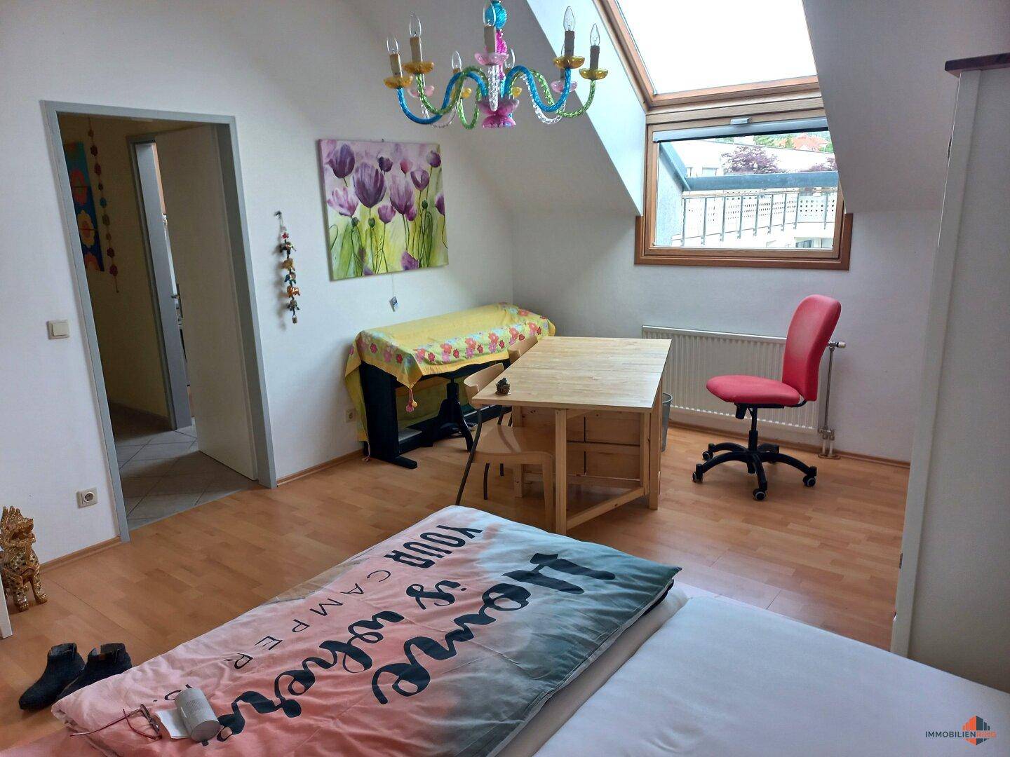 Helles Schlafzimmer im Dachgeschoss mit Holzboden, Dachfenster und farbenfroher Dekoration.