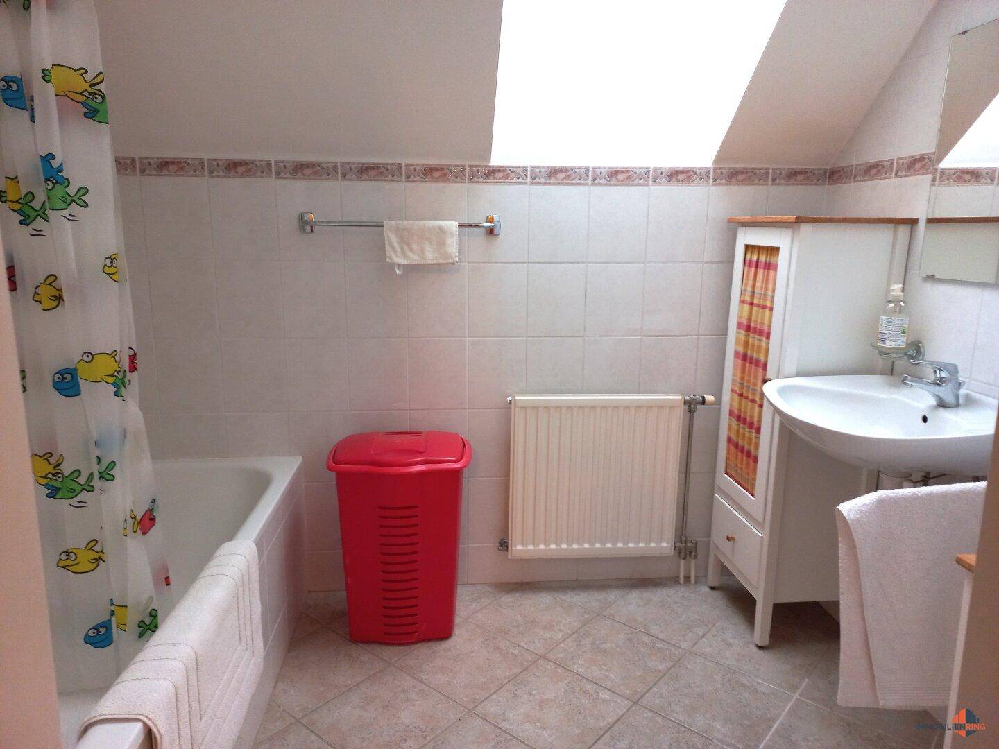 Helles Badezimmer mit Badewanne, Waschbecken und Dachfenster, ausgestattet mit Fliesenboden.