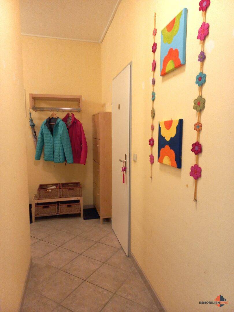 Gemütlicher Flur mit gelben Wänden, Fliesenboden und Garderobe, dekoriert mit bunten Bildern.