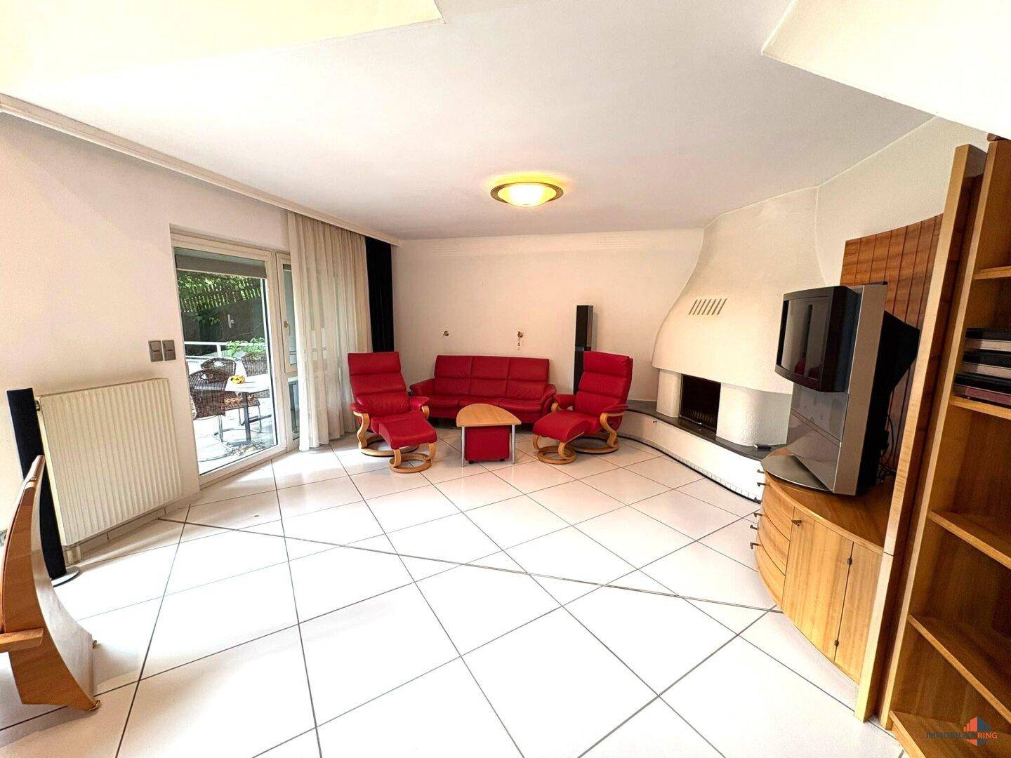 Gemütliches Wohnzimmer mit Kamin, Fliesenboden und Zugang zur Terrasse.