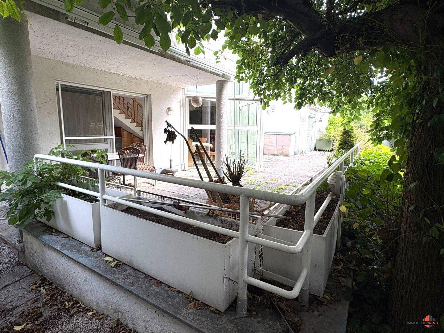 Überdachte Terrasse mit Pflanzenkübeln und Treppenzugang zum Gartenbereich.