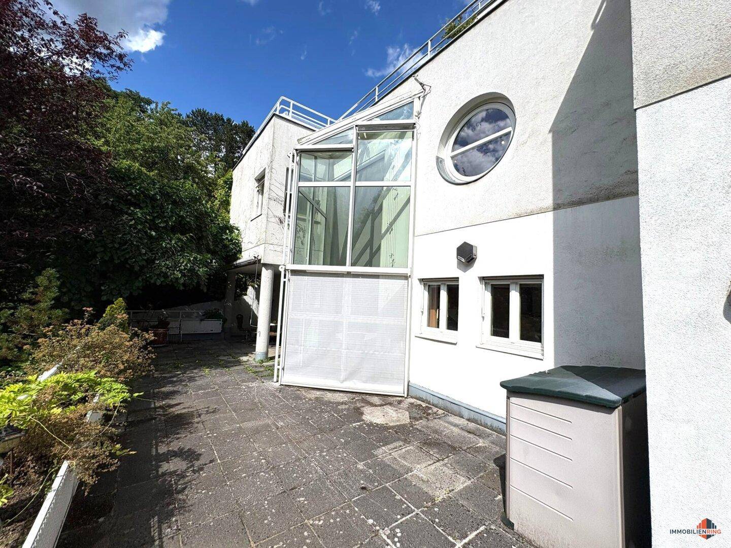 Seitlicher Außenbereich mit gepflasterter Terrasse und moderner Glasfassade.