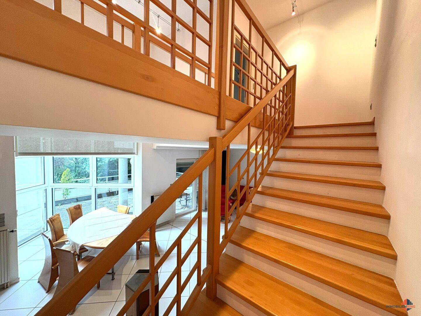 Elegante Holztreppe führt zu einer offenen Galerie mit Blick auf den Wohnbereich.