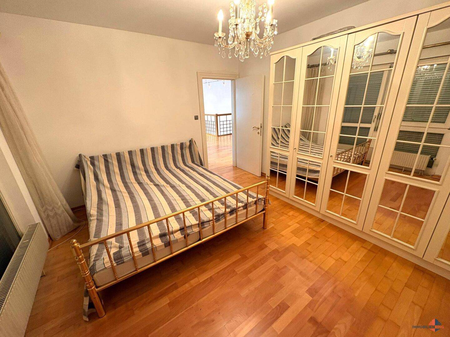Schlafzimmer mit Holzfußboden, Spiegelschränken und Kronleuchter.