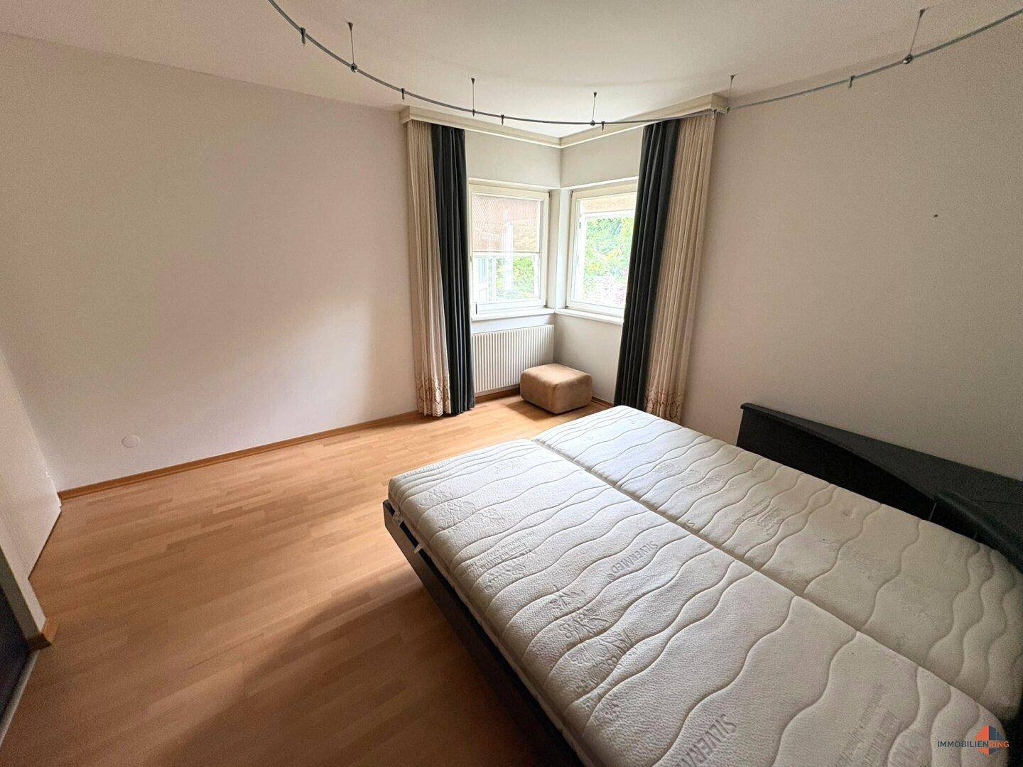 Helles Schlafzimmer mit Eckfenstern, Holzfußboden und viel natürlichem Licht.