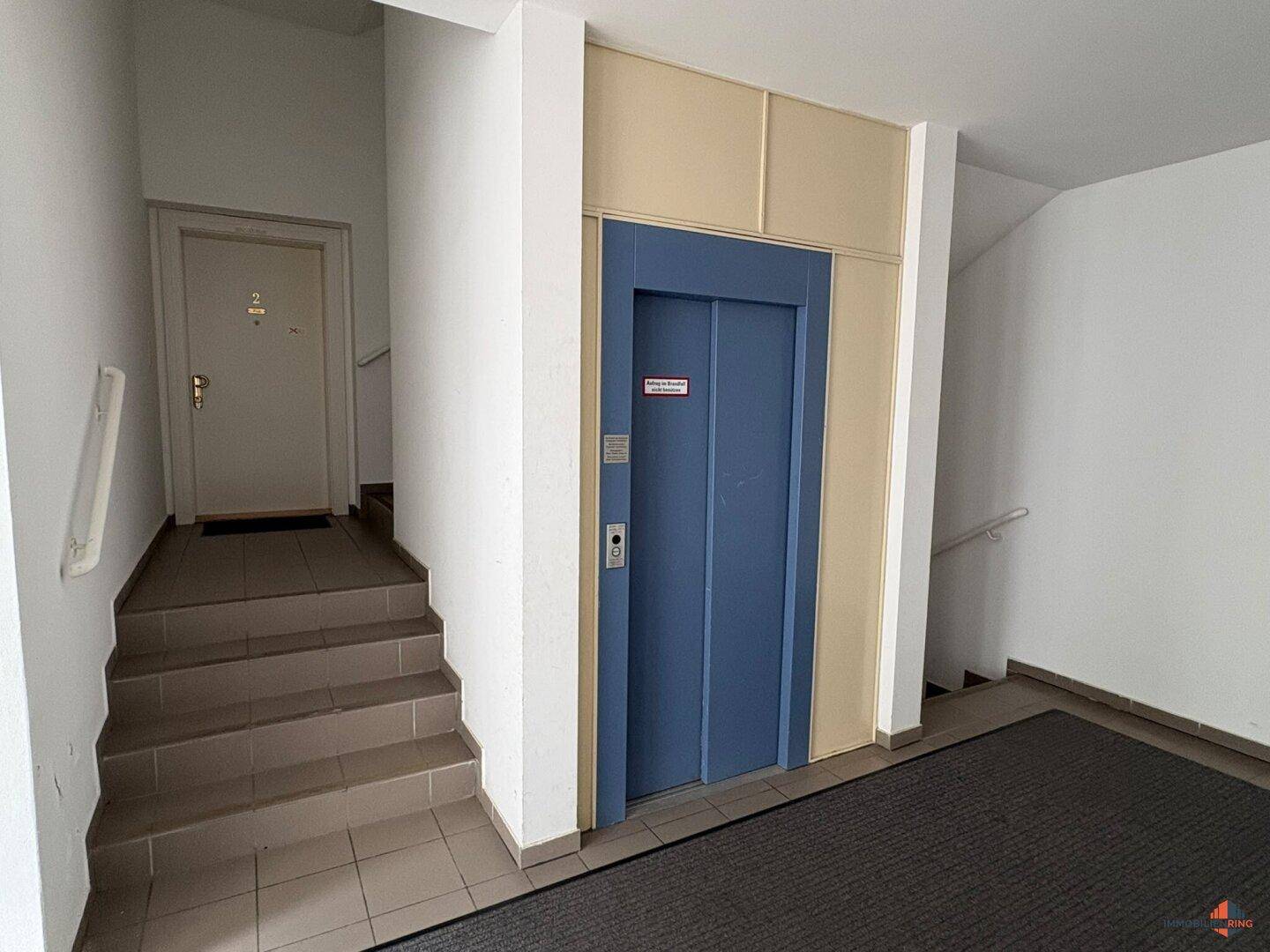 Heller Flur mit Aufzug, Treppenhaus und Zugang zu den Wohneinheiten.