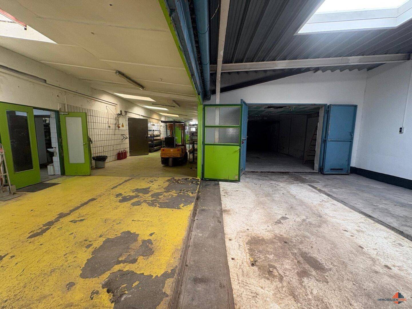 Große Lagerhalle mit gelb-grün gestrichenem Betonboden und einem Gabelstapler im Hintergrund.