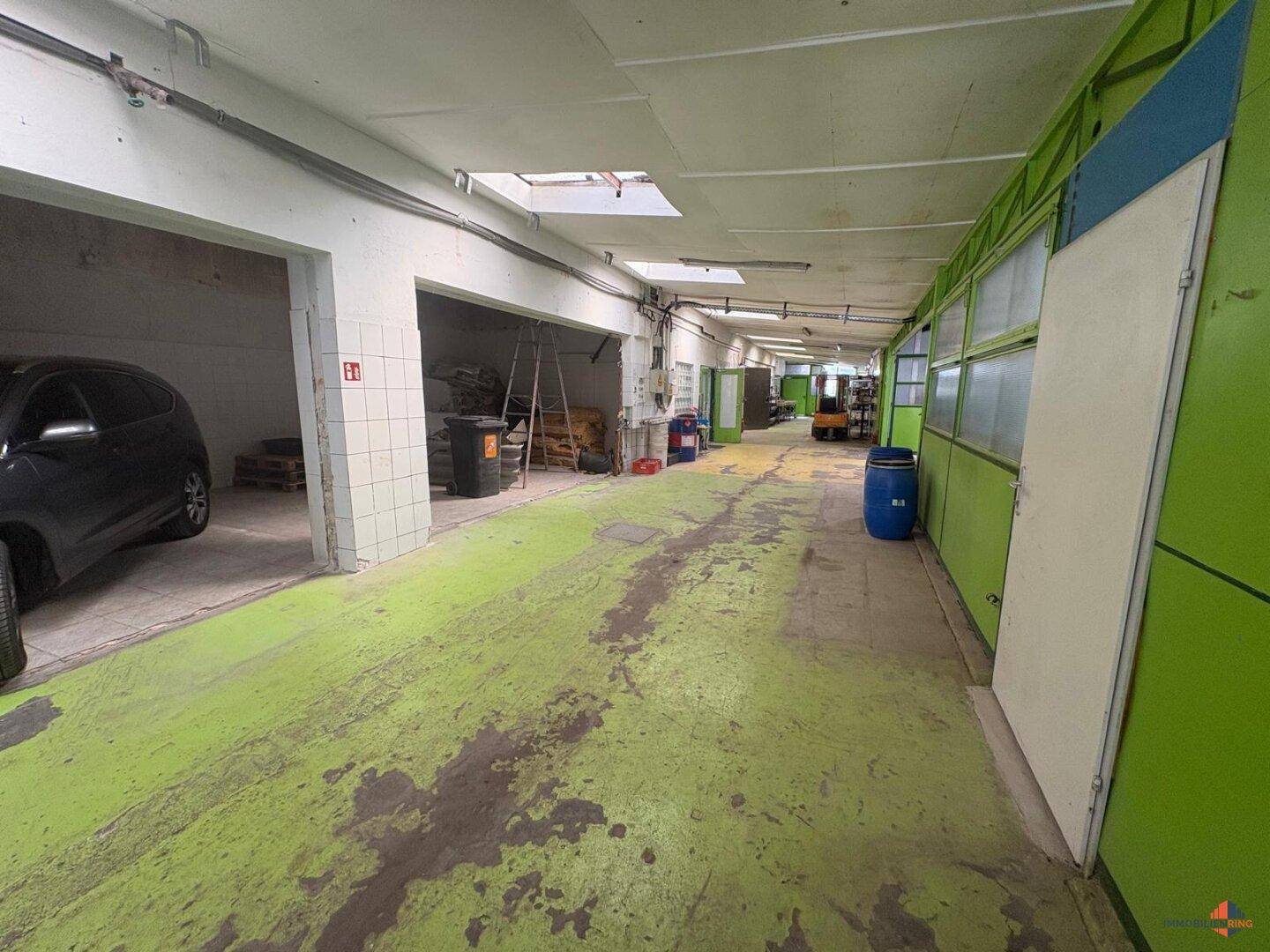Langer Lagerraum mit grün gestrichenem Betonboden, Oberlichtern und einem geparkten Auto.
