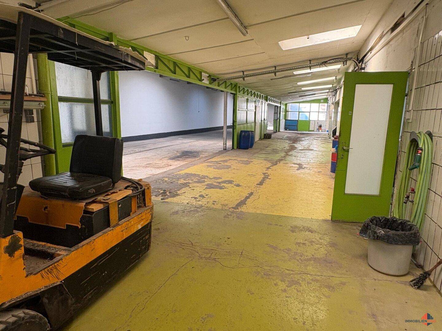 Industrieller Lagerraum mit gelb-grünem Boden, Gabelstapler und Oberlichtern für Tageslicht.