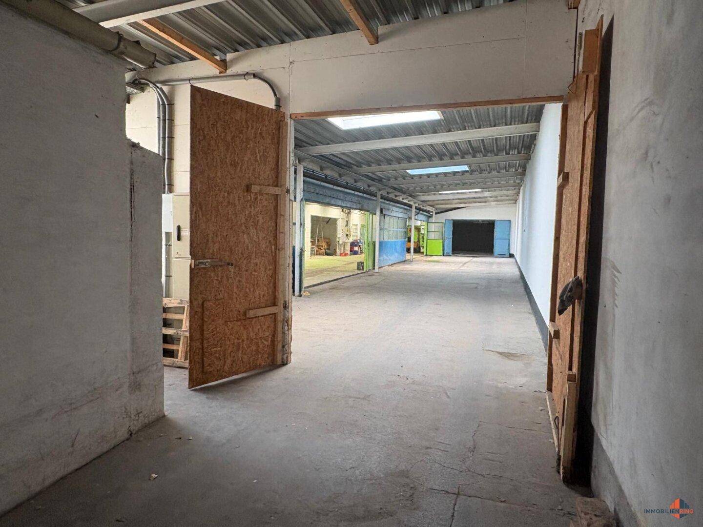 Geräumige Lagerhalle mit Betonboden und großen Holztüren, die zu weiteren Bereichen führen.