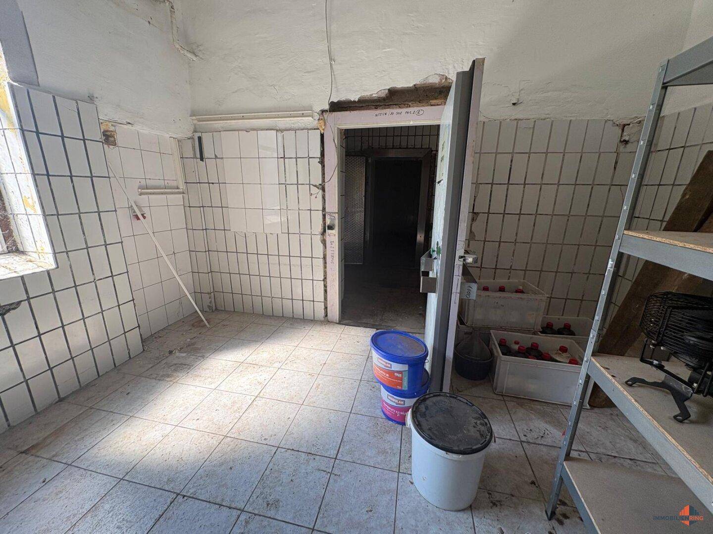 Lagerraum mit weißen Wandfliesen und einem Fenster, der auf eine Renovierung wartet.