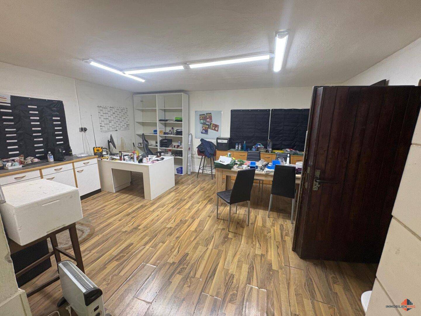 Büroraum mit Laminatboden, Regalen und Schreibtischen, ausgestattet für den Arbeitsalltag.