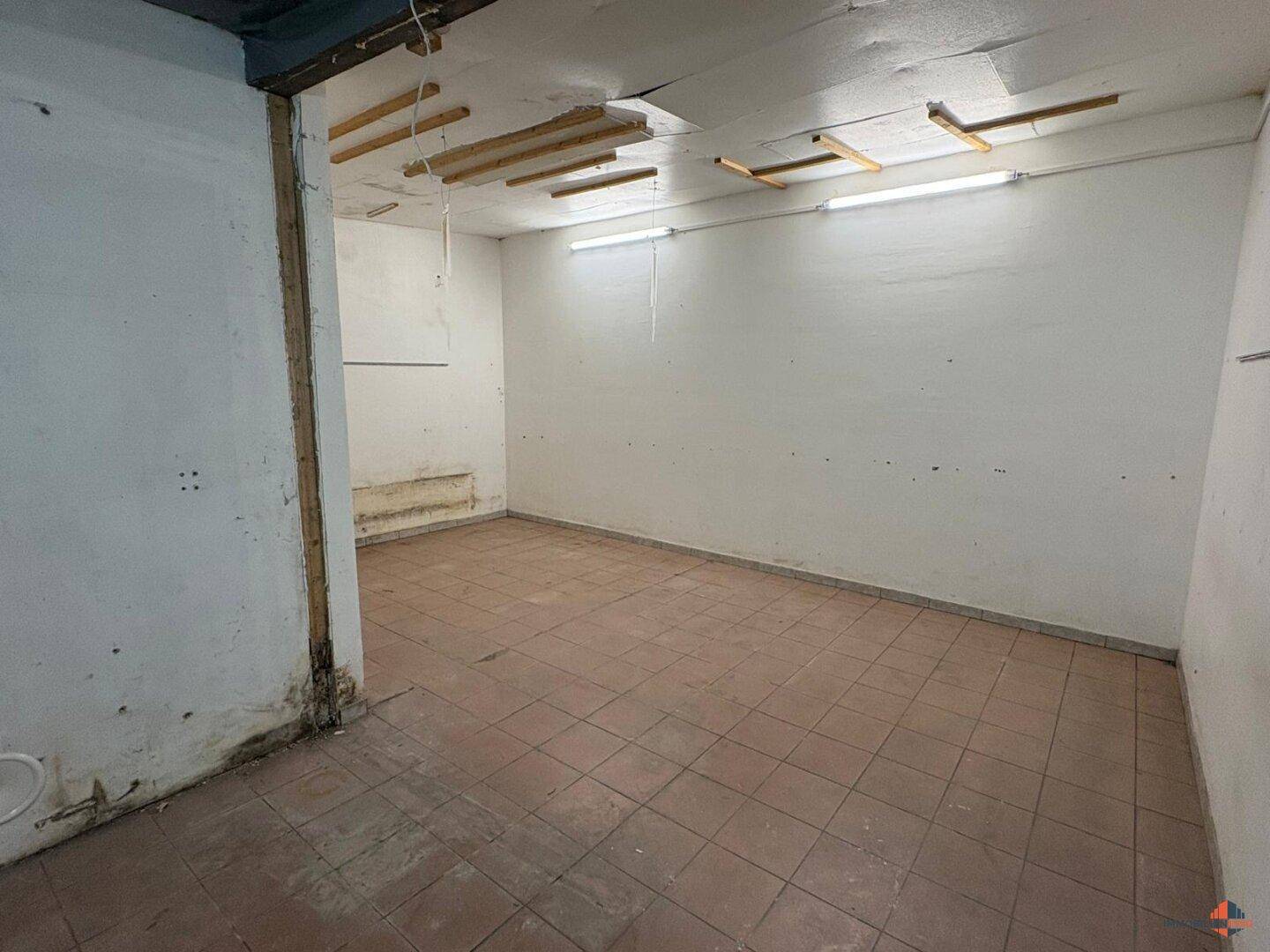 Leerer Raum mit Terrakotta-Fliesenboden und einfacher Beleuchtung, ideal als Abstellraum.