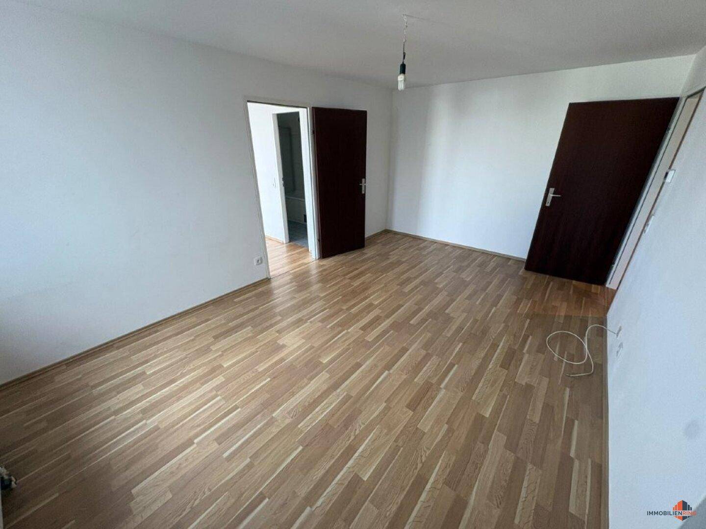 Leerer Raum mit hellem Parkettboden und weißen Wänden, bereit zur individuellen Gestaltung.