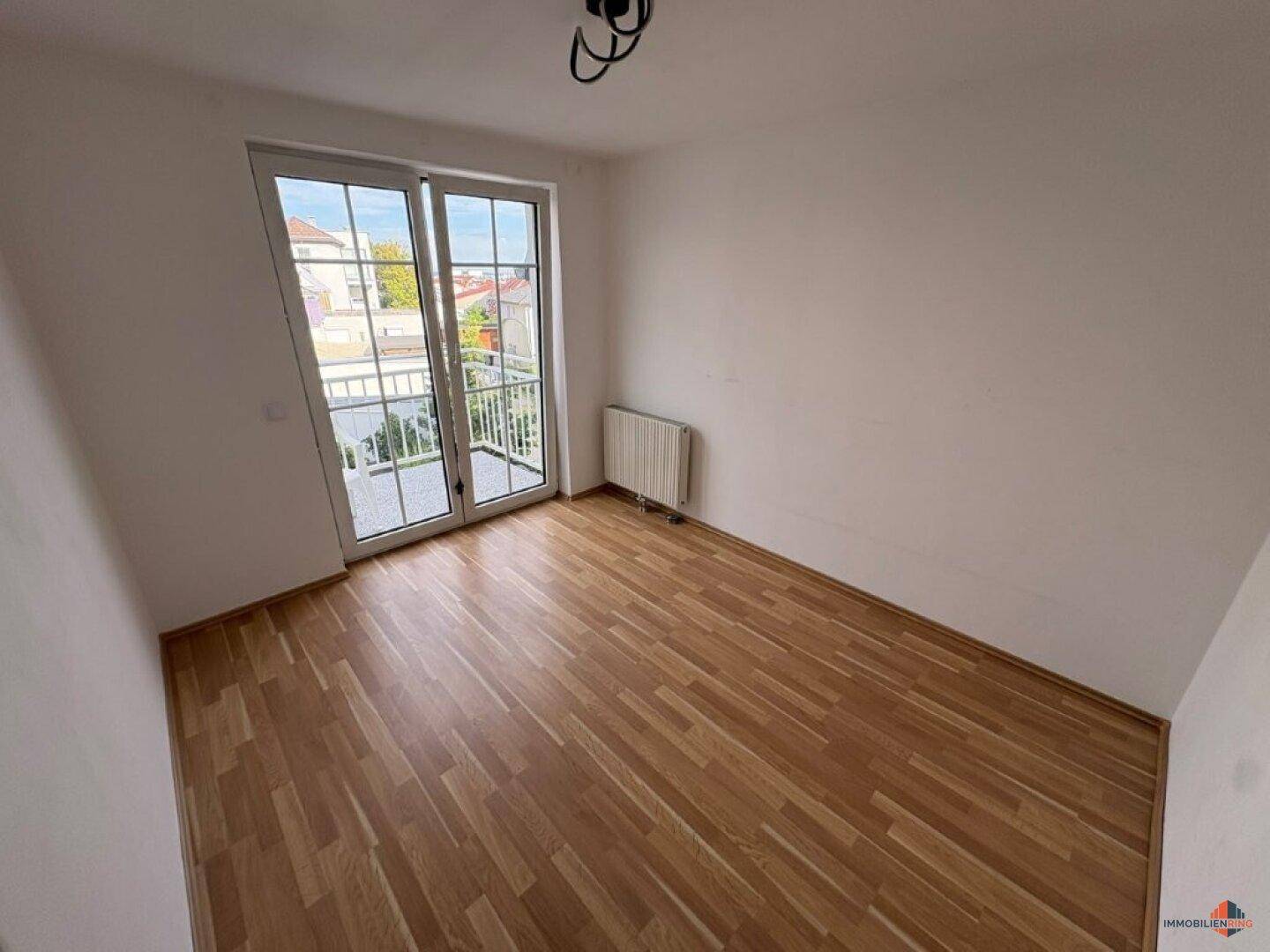 Heller Raum mit Parkettboden und Balkonzugang, ideal für Schlaf- oder Wohnbereich.