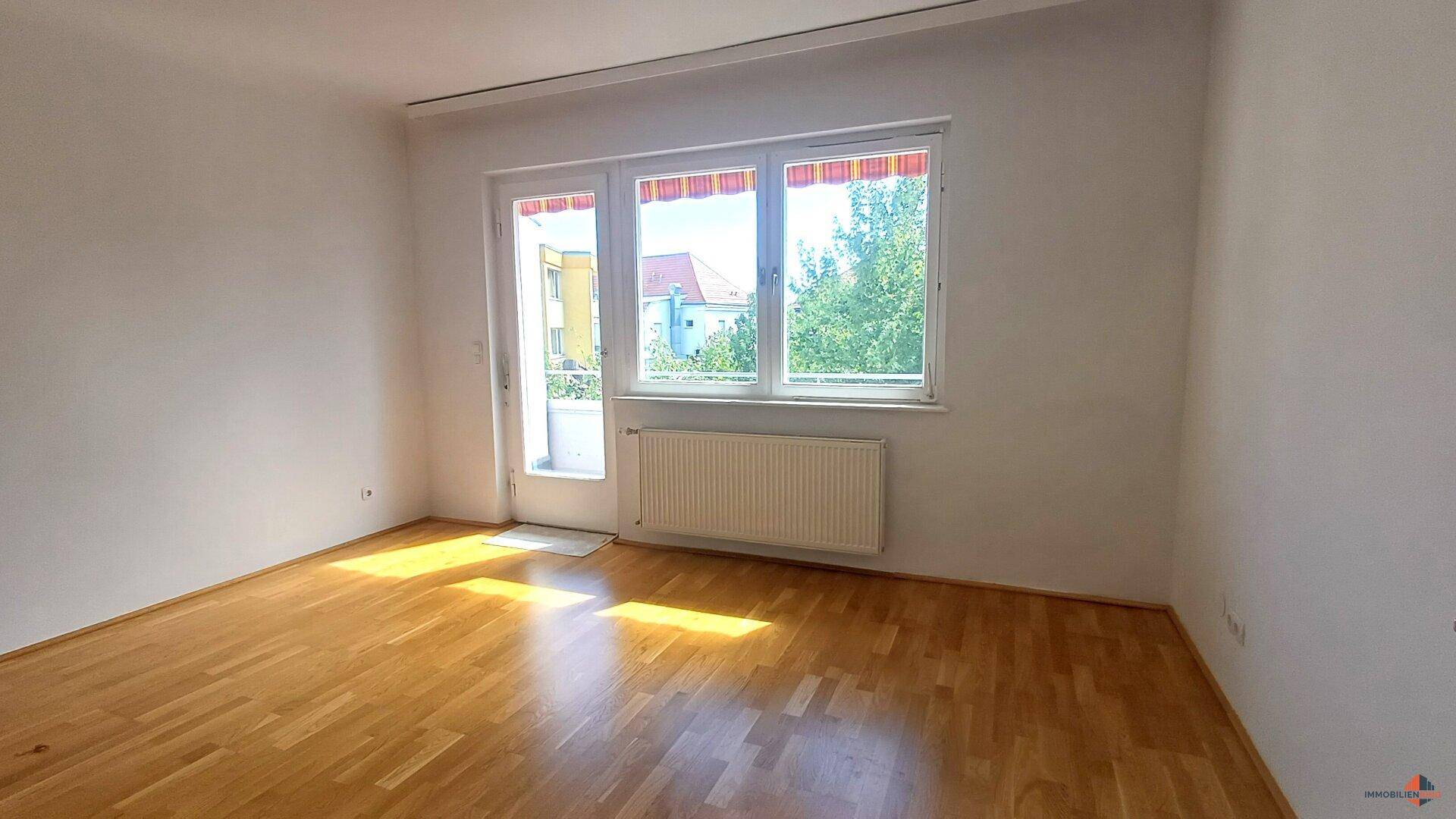 Lichtdurchfluteter Raum mit Parkettboden und Zugang zu einem Balkon.