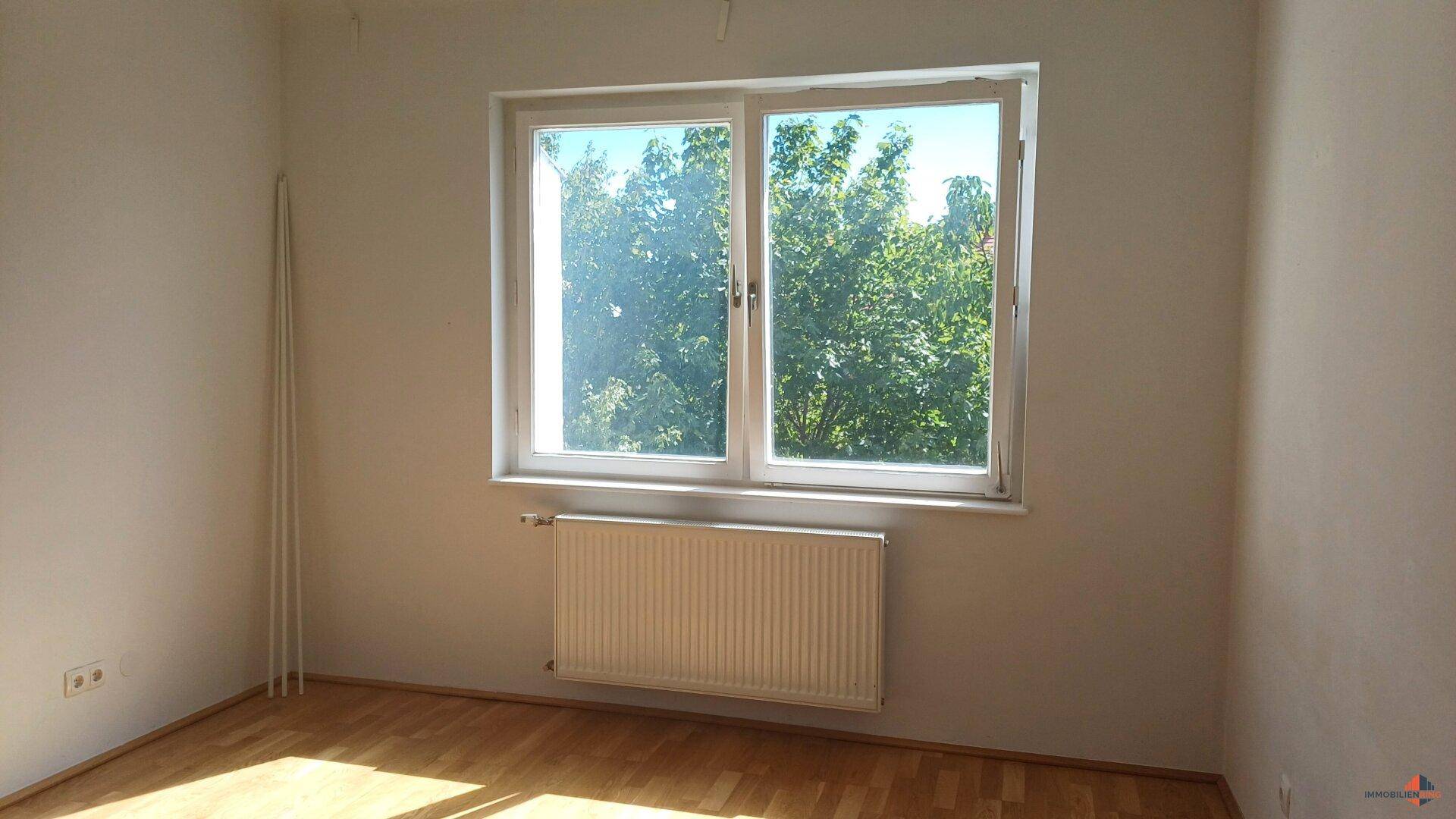 Helles Zimmer mit Parkettboden und Blick auf grüne Bäume.