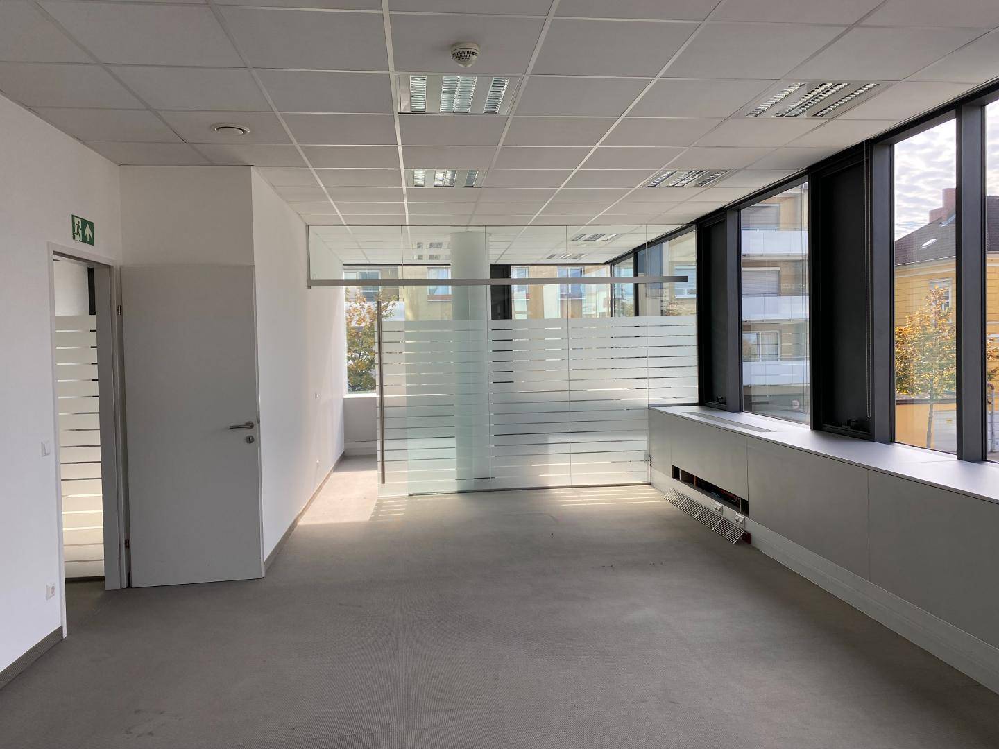 Offener Bürobereich mit Glaswänden, großen Fenstern und einem Ausgang, der viel natürliches Licht bietet.