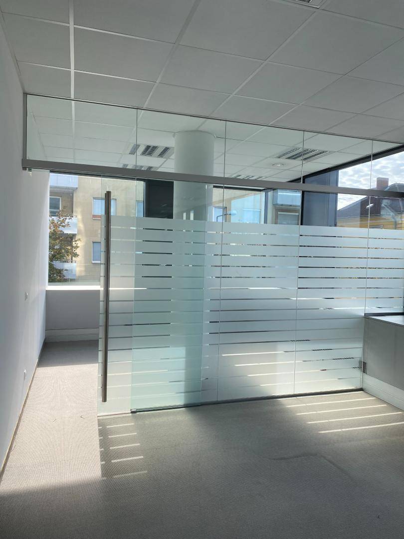Bürobereich mit einer Glaswand, die Privatsphäre schafft, und großen Fenstern, die Tageslicht hereinlassen.