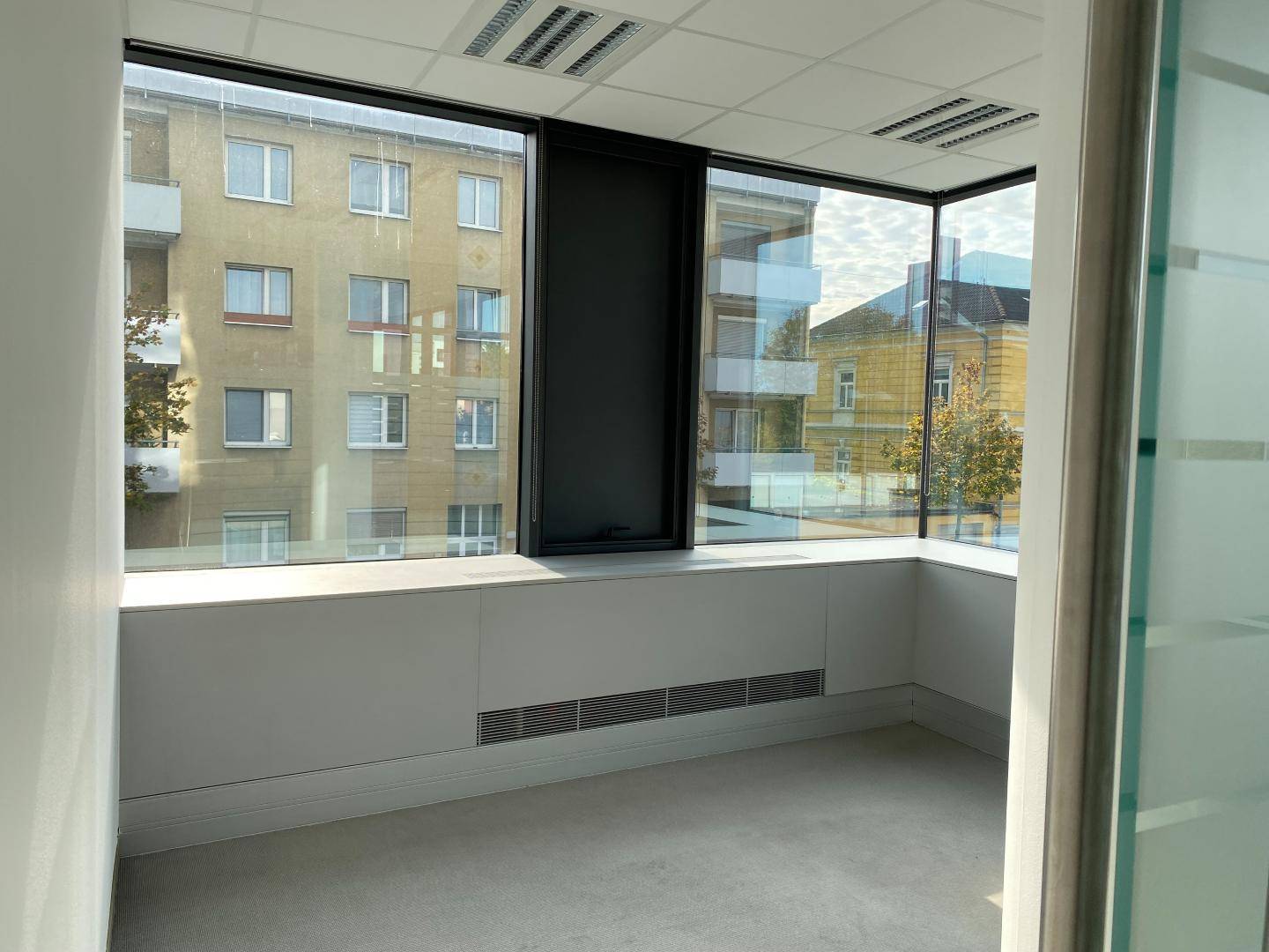 Eckbüro mit großen Fenstern, die einen weiten Blick auf die Umgebung bieten, und einem Teppichboden.