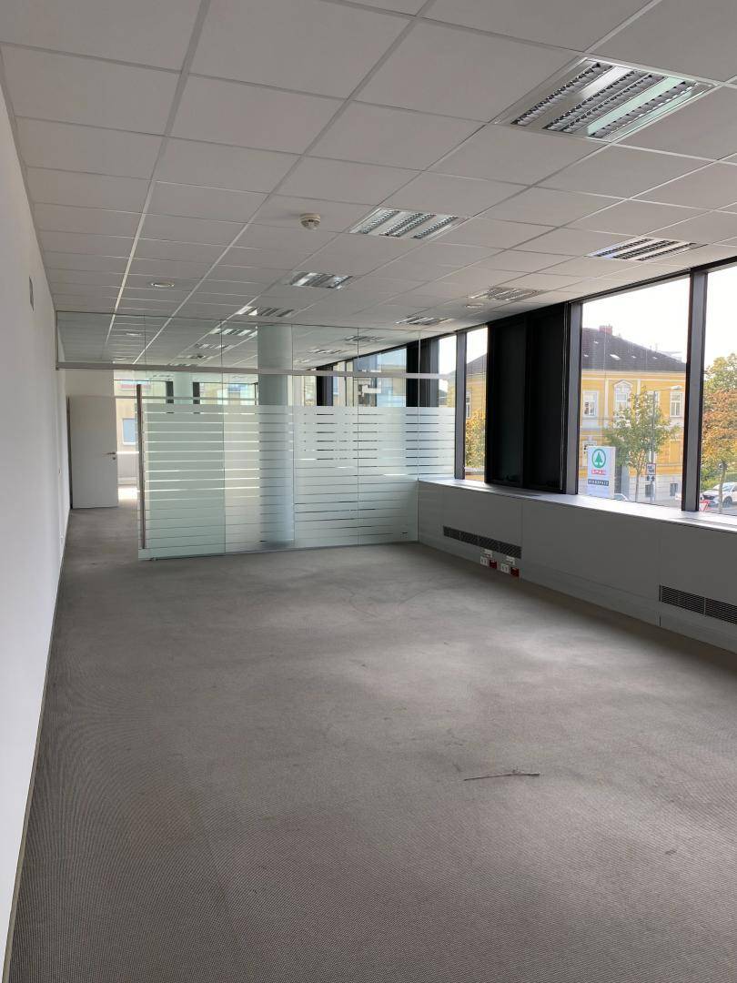 Offener Bürobereich mit Glaswänden, großen Fenstern und Vinylboden, der eine flexible Raumgestaltung ermöglicht.