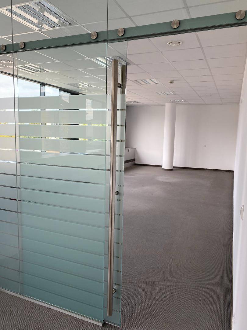 Blick durch eine Glastür in einen offenen Bürobereich mit Vinylboden und einer zentralen Säule.