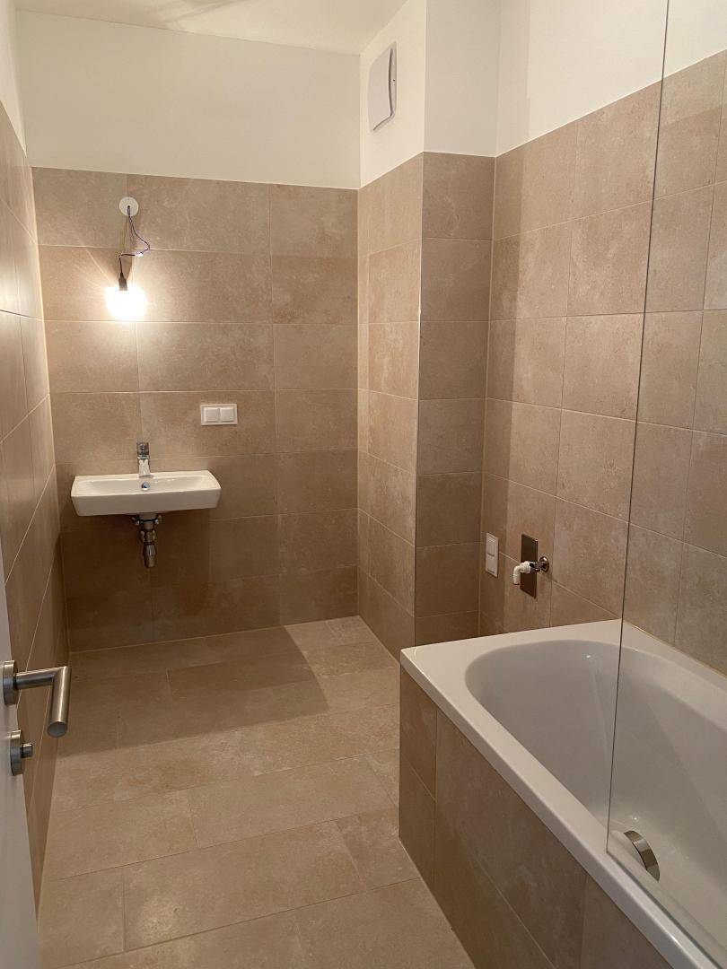 Modernes Badezimmer mit beigefarbenen Fliesen, Badewanne und Waschbecken.