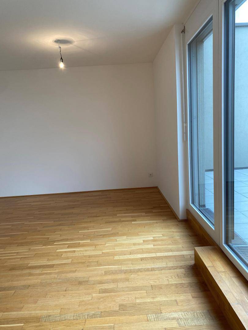 Heller Wohnbereich mit Holzboden und bodentiefen Fenstern, die viel Tageslicht hereinlassen.