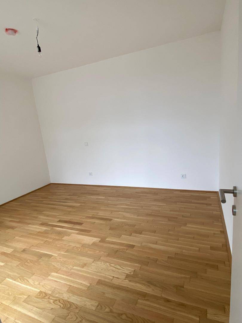 Helles Schlafzimmer mit Parkettboden und weiß gestrichenen Wänden, bereit zur Einrichtung.