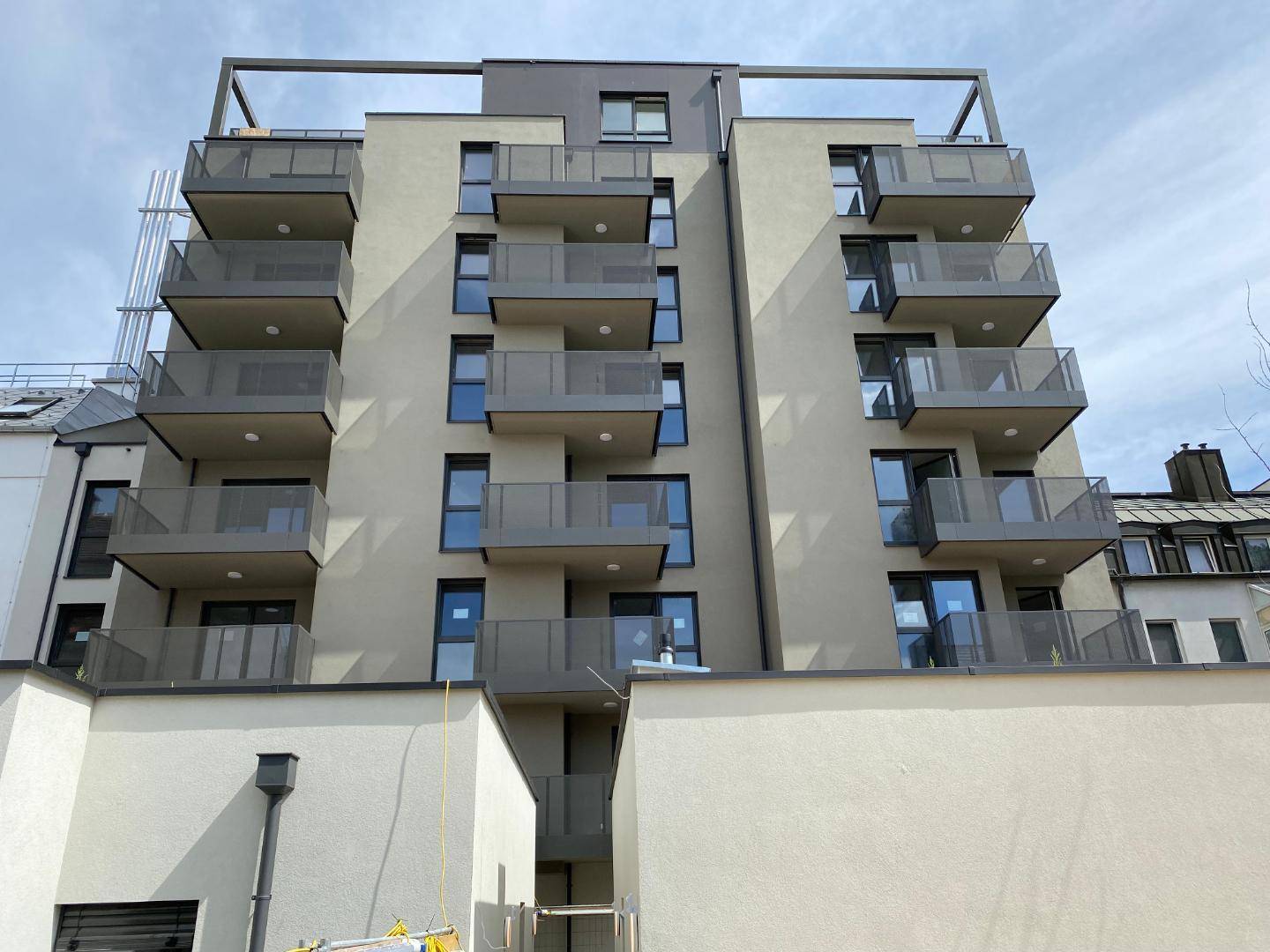 Moderne Wohnhausfassade mit zahlreichen Balkonen und großen Fenstern unter blauem Himmel.