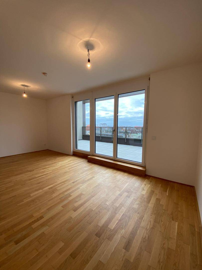 Geräumiger, heller Wohnraum mit Parkettboden und Zugang zu einer großen Terrasse.