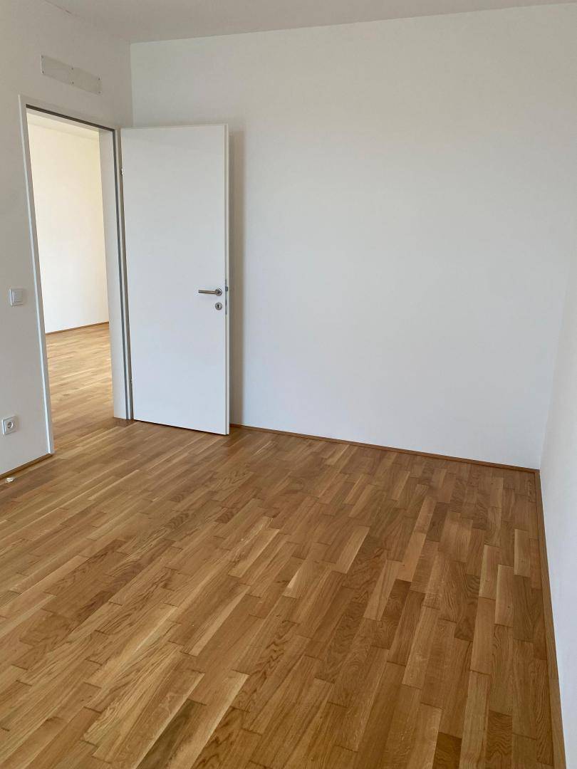 Helles Schlafzimmer mit Holzboden und weißer Tür, bietet direkten Zugang zum Flur.