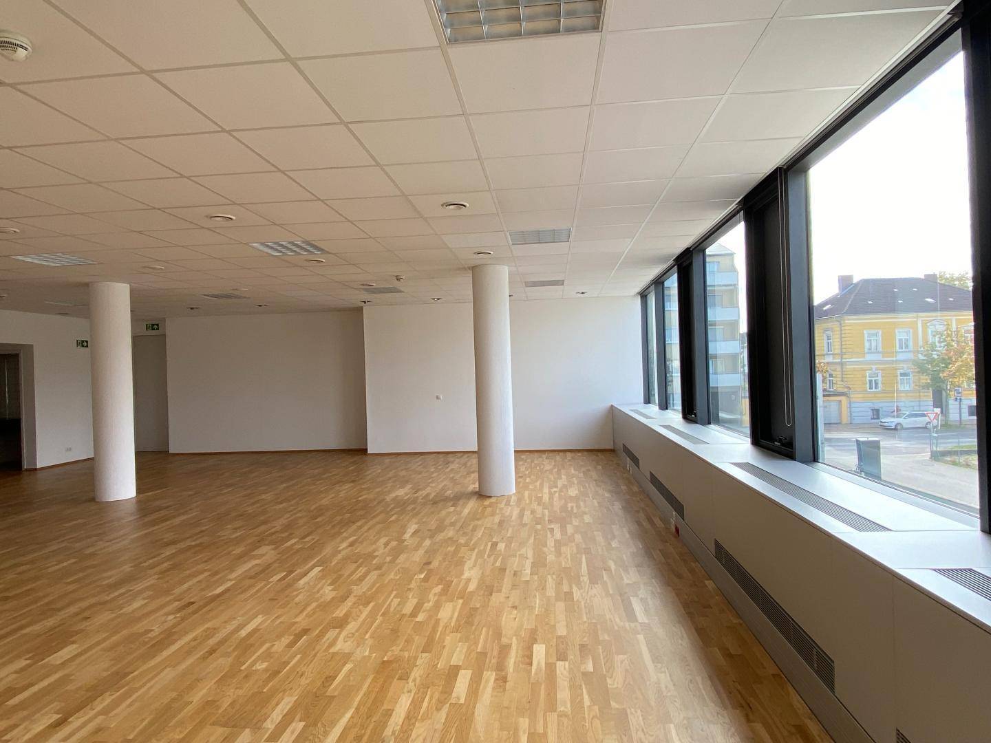 Heller Büroraum mit durchgehenden Fenstern, die einen Blick auf die Stadt und die umliegenden Gebäude bieten.